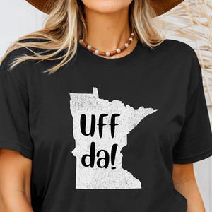 May include: Black t-shirt with a white outline of the state of Minnesota and the text "UFF da!" printed on it.