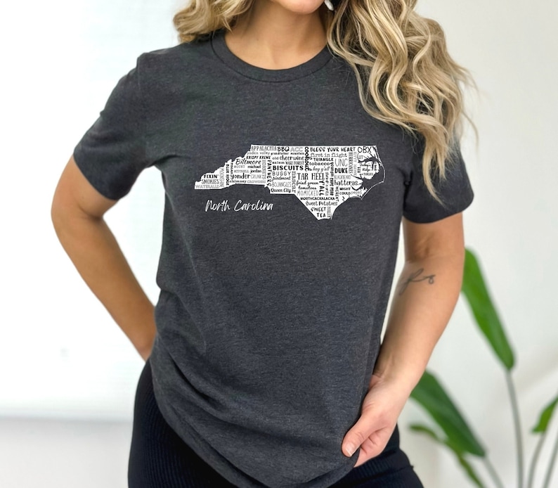 Pu&ograve; includere: Una maglietta grigia melange scuro con un contorno bianco dello stato della Carolina del Nord. Il contorno &egrave; riempito con parole relative alla Carolina del Nord, come "Tar Heels", "Biscuits", "BBQ" e "Duke". Le parole "North Carolina" sono stampate sotto il contorno.