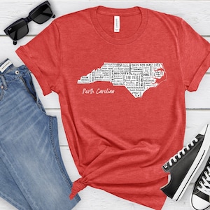 Pu&ograve; includere: Maglietta rossa con un contorno bianco dello stato della Carolina del Nord. Il contorno &egrave; riempito con parole relative alla Carolina del Nord, come "Tar Heels", "Duke", "Biscuits", "Smokies", "Yonder" e "Appalachia".