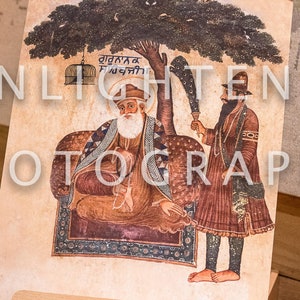 May include: An illustrated artwork featuring two figures under a tree, displayed on a wooden easel. The artwork shows detailed figures in traditional attire, with text at the top. The easel is made of light-coloured wood with brass hardware.