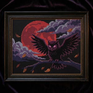May include: Cross-stitch art of an owl with outstretched wings perched on a branch. The owl is black with glowing purple eyes, set against a red moon and dark sky. The framed artwork includes autumn leaves and clouds.