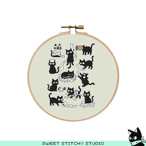 May include: A cross-stitch embroidery hoop featuring a playful design of black cats in various poses. The cats are depicted with simple, cartoon-like features, interacting with objects like toilet paper rolls and crowns. The hoop is made of wood and has a light beige fabric background.