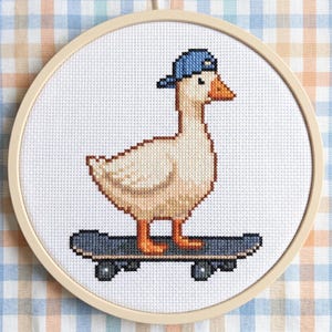 May include: Cross-stitch embroidery of a goose wearing a blue baseball cap and standing on a skateboard. The goose is white with brown outlines and orange feet and beak. The skateboard is dark blue. The embroidery is in a round wooden hoop.