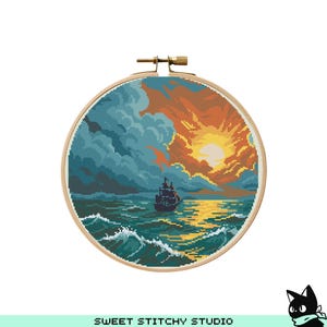 May include: A cross-stitch embroidery in a wooden hoop depicts a seascape with a ship sailing on turquoise waves under a dramatic sky. The sky transitions from stormy blue to a vibrant orange sunset. The text "SWEET STITCHY STUDIO" is at the bottom.