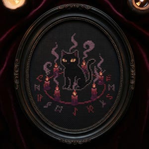 Puede incluir: Un bordado en punto de cruz enmarcado que representa un gato negro rodeado de velas y humo. El gato tiene ojos amarillos y está dentro de un círculo de velas. El marco es ovalado y oscuro, con un borde decorativo.