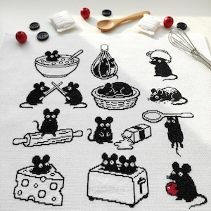 以下が含まれることがあります： キッチン用品と交流するネズミの様々なシーンを描いた、白黒のクロスステッチデザイン。デザインには、ボウル、ボトル、バスケット、めん棒の中のネズミが含まれています。追加の要素には、赤いビーズ、黒いボタン、木のスプーンが含まれています。
