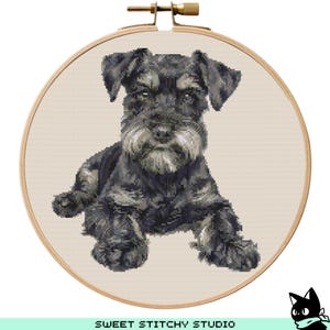 Puede incluir: Un patrón de punto de cruz de un perro schnauzer miniatura negro y gris en un aro de bordado de madera.