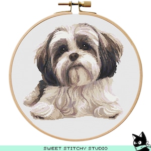Op de afbeelding: Een kruissteekpatroon van een Shih Tzu hond met bruin en wit haar. De hond ligt met zijn kop op zijn poten. Het patroon is op een witte achtergrond.