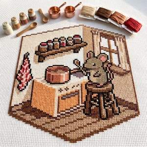 May include: Cross-stitch art depicting a mouse cooking in a kitchen. The scene includes a stove, copper pots, spice jars, and a small stool. The color palette features shades of brown, beige, and red. Additional items include wooden spoons and spools of thread.