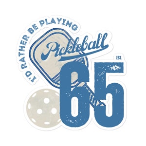 Puede incluir: Un diseño de pegatina con la palabra "Pickleball" en escritura cursiva, el texto "I'd rather be playing" y el número "65". El diseño incluye una pala y una pelota de pickleball en tonos azules y beige.