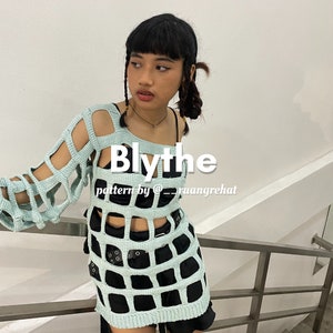 Peut inclure: Une femme portant un haut en crochet bleu clair avec une jupe noire et une ceinture noire. Le haut a un motif en grille large et le texte "Blythe pattern by @ruangrehat" est imprimé sur le devant.