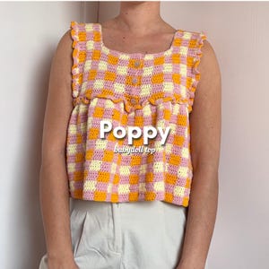May include: A sleeveless, crochet top in a gingham pattern of yellow, orange, and pink. The top has a square neckline, decorative buttons, and ruffled edges. The word "Poppy" and "babydoll top" are printed on the front.