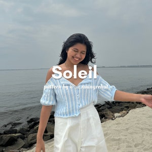 以下が含まれることがあります： 肩出しのデザインの薄い青と白のストライプのクロシェトップを着た女性。トップはボタン留めで、白いパンツと合わせています。青い背景に白い文字で「Soleil」と書いてあり、その下に「pattern by @ruangrehat」と書いてあります。