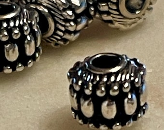 May include: Silver bead with a textured design featuring small, rounded bumps and a central hole. The bead has a silver finish and a slightly rounded shape.