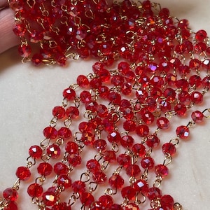 May include: A strand of red crystal beads strung on a gold chain. The beads are faceted and have a slight iridescent shimmer.