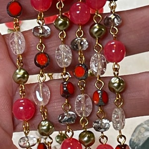 May include: A multi-strand necklace with pink, clear, and green beads. The necklace features a gold chain and a variety of bead shapes and sizes.