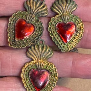 May include: Three vintage-style heart-shaped pendants. Each pendant features a red heart center, surrounded by a green border with gold accents. The pendants have a loop at the top for hanging.