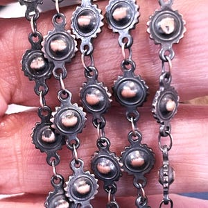 May include: A close-up of a silver chain with copper-toned round beads. The chain is made of small, linked circles with a decorative design. The beads are slightly raised and have a smooth, shiny finish.