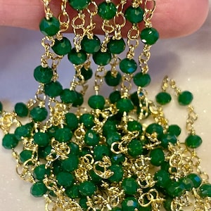 May include: A close-up of a gold chain with green faceted beads. The chain is made of small, delicate links and the beads are evenly spaced.