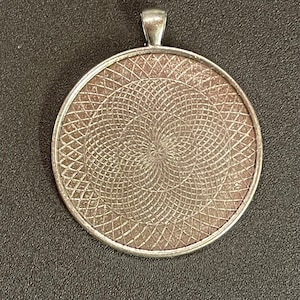 May include: Silver pendant with a circular design featuring a geometric pattern of intersecting lines.