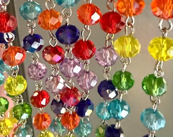 May include: A close-up of multiple strands of colourful, faceted beads. The beads are in a rainbow of colours, including red, orange, yellow, green, blue, and purple. They are strung together with silver-coloured metal links, creating a decorative effect. The beads are likely glass or crystal.
