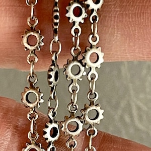 May include: A silver chain necklace with multiple strands of small, circular, gear-shaped links.