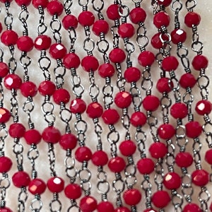 May include: A strand of red faceted beads strung on a silver chain. The beads are small and round, and the chain is delicate.