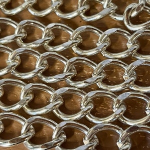 May include: Close-up of a silver chain with oval links. The chain is lying on a wooden surface.