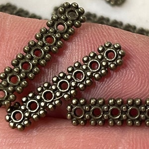 May include: A close-up of several antique gold-toned metal spacers with a decorative design of small circles and dots. The spacers are about 1 inch long.
