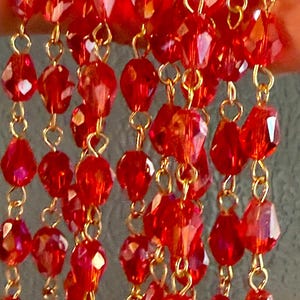 May include: Close-up of strands of red faceted beads with gold-colored chain links. The beads are various shapes and sizes, reflecting light. The jewelry is likely for a necklace or other decorative accessory.