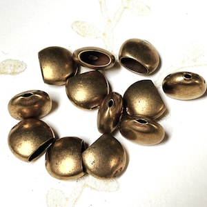 May include: A collection of ten antique gold-toned metal beads with a smooth, slightly textured finish. The beads are oval-shaped with a hole in the center.