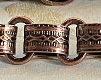 May include: Close-up of a copper chain bracelet with a detailed, patterned design. The chain links are connected with a circular loop.