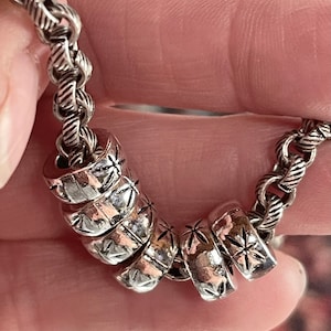 May include: A silver chain necklace with multiple silver beads. The beads are round and have a star-shaped design.