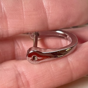 May include: A silver-toned metal buckle with a smooth, curved design. The buckle has a small hole on one side and a screw on the other.