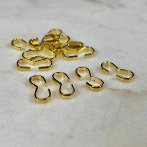 May include: A pile of gold-colored metal jump rings, some are open and some are closed. The jump rings are small and are used for jewelry making.