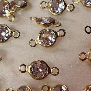 May include: A group of gold-tone metal connector charms with clear crystal stones. Each charm has two loops for attaching to jewelry.