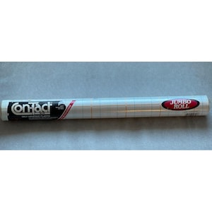 May include: A roll of Contact brand self-adhesive plastic shelf liner. The roll is white with a grid pattern and has a red and white "Jumbo Roll" label. The Contact brand logo is visible on the packaging.
