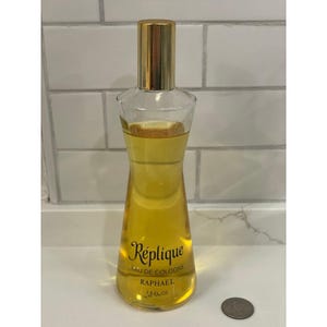 May include: A clear glass bottle of Réplique Eau de Cologne by Raphael, with a gold-colored cap. The bottle contains a yellow liquid and has the text "Réplique Eau de Cologne" and "Raphael" printed on it. The bottle is 7.5 fl oz.