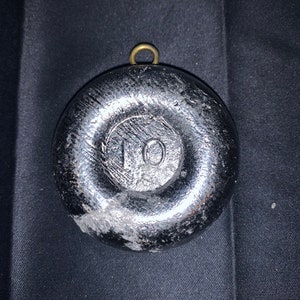 May include: A silver-colored fishing sinker with a brass loop at the top. The sinker is round and has a raised number "10" on the front.