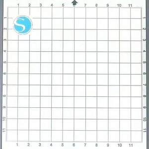 May include: A white cutting mat with a grid pattern and a blue logo in the upper left corner. The grid is divided into 1-inch squares, with numbers along the edges for precise measurements. An arrow indicates the top.