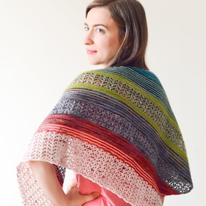 May include: A woman wearing a colorful striped and lacy shawl with a white crocheted border. The shawl is made with a variety of colors, including red, green, blue, and purple.