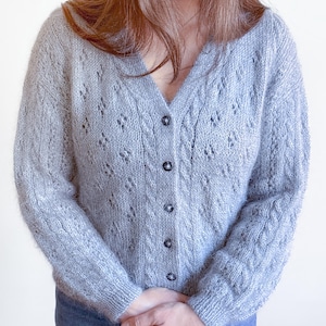 May include: A light grey knitted cardigan with a V-neck and button fastening. The cardigan features a delicate openwork pattern.