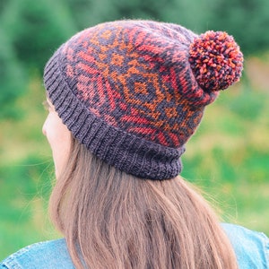 May include: A knitted hat with a pom-pom on top. The hat is brown, orange, and red with a geometric pattern.