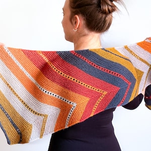 Peut inclure: Un châle en tricot rayé coloré avec un motif géométrique. Le châle est fait avec une variété de couleurs de fil, y compris l'orange, le rouge, le jaune, le gris et le blanc.