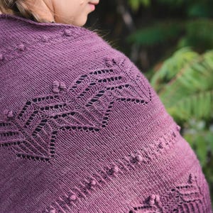 May include: A knitted shawl in a deep purple hue, featuring intricate openwork and textured bobbles. The shawl's design includes geometric patterns and a ribbed border, offering a cozy and stylish accessory.