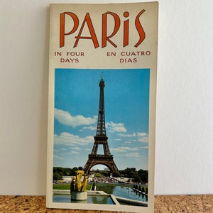 以下が含まれることがあります： フランスのパリへのヴィンテージ旅行ガイドで、表紙にはエッフェル塔の写真が掲載されています。表紙はオレンジと白で、「パリ」という文字が大きく太字でオレンジ色で書かれています。表紙には「In Four Days」と「En Cuatro Dias」という文字も書かれています。