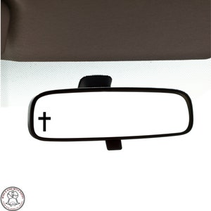May include: A black rearview mirror with a small black cross sticker on the left side of the mirror.