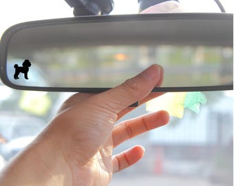 May include: A black silhouette of a poodle dog sticker on a rearview mirror in a car.