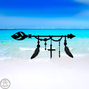 May include: Black metal arrow-shaped wall decor with a feather and cross design. The arrow has a leaf-shaped end and a pointed tip. The design includes hanging feathers, hearts, and diamond shapes. The background is a beach scene with blue sky and water.