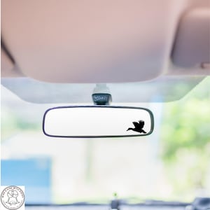 May include: A black silhouette of a bird flying in front of a rearview mirror in a car.